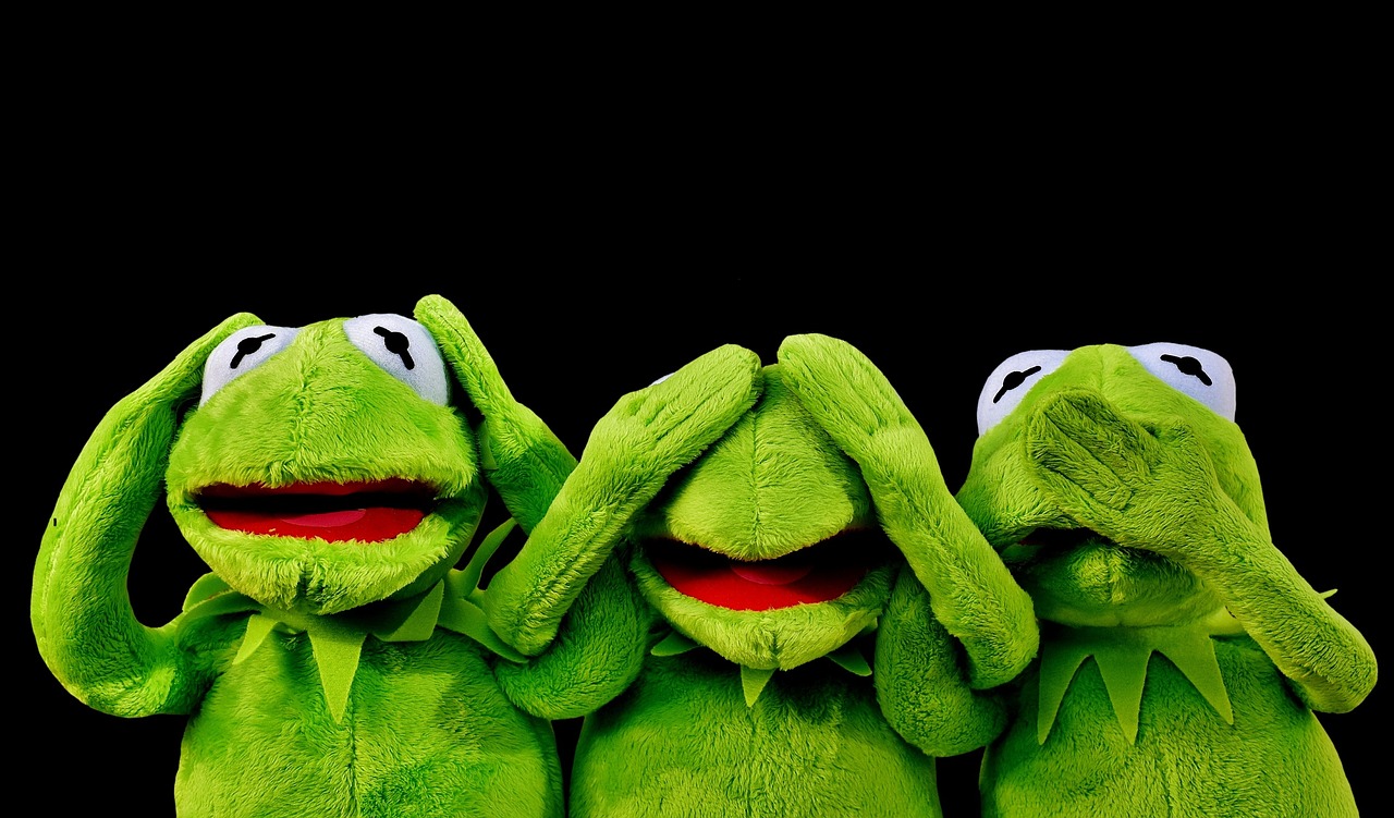 3 Kermit-Stoffpuppen (Frösche) halten sich vor schwarzem Hintergrund die Augen, Ohren und den Mund zu